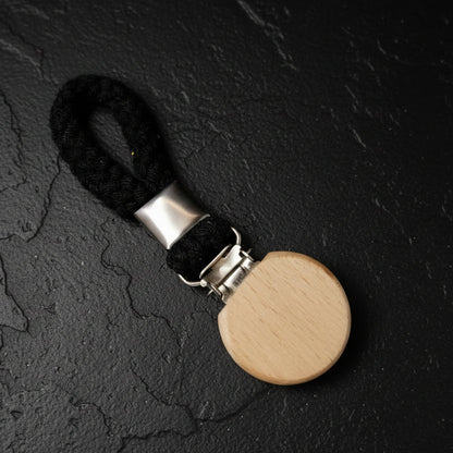 Wooden round towel clip with a black strap on a dark textured surface