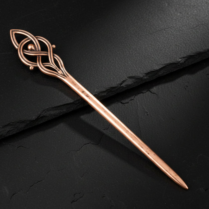 Copper hairpin with intricate design on a dark gray background