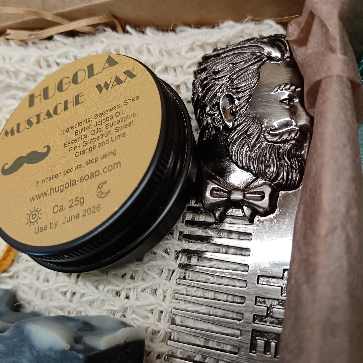 Hugola mustache wax container with decorative lid featuring a mustache design, placed on a textured surface.