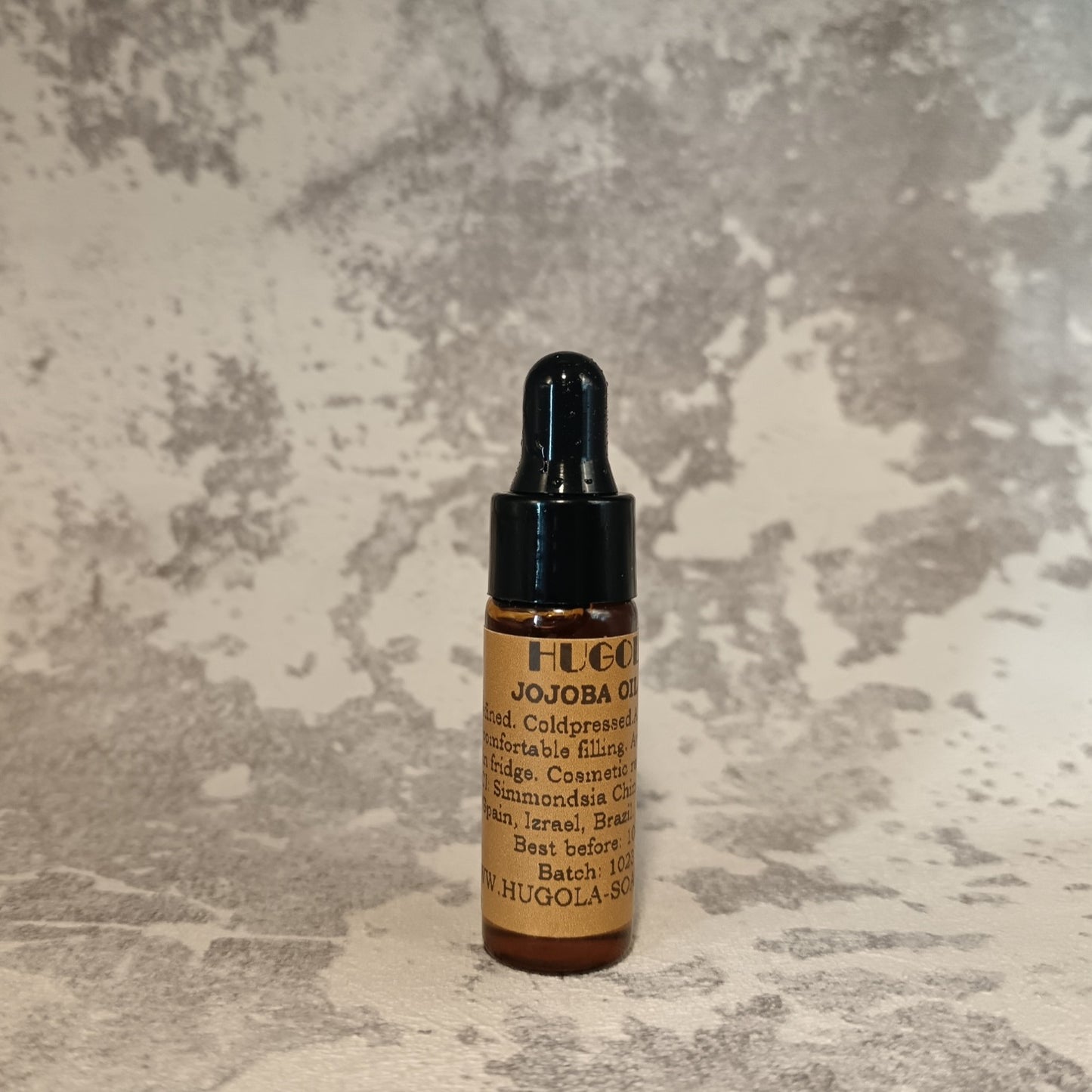 5ml jojoba oil mini bottle for natural skin hydration on a textured background