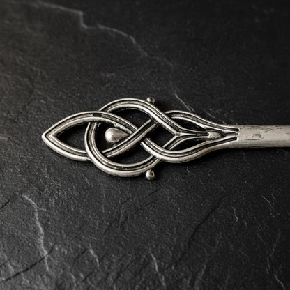 Silver hair clip with intricate design on a dark gray background